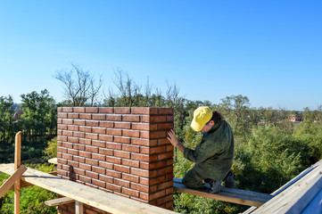 Worker on the roof lays a pipe of brick.