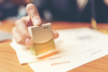 Close-up Of A Person's Hand Stamping With Approved Stamp On Document At Desk