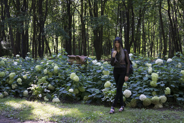Girl wears hood and backpack in park near flowers of hortensia