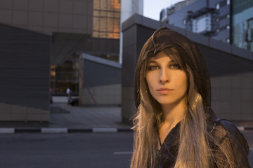 Fototapeta na wymiar Portrait of a fashion urban girl wear black hood in the cityscape in warm light close up