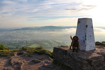 Morning view across the countryside at sunrise with fog and clouds of dog and trig point