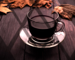Tea and maple leaves on a black wooden table with a shadow from the window