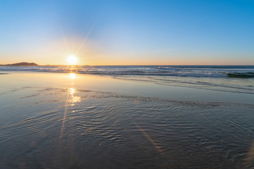 Fototapeta na wymiar Sunrise star burst over the beach with shiny wet sand in the foreground, NSW, Australia