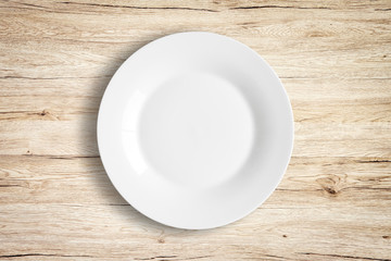 Top view of empty white food plate on a wood background.