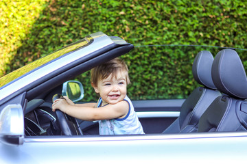 Cute happy smiling little baby boy holding the steering wheeel and driving cabriolet car. Little...
