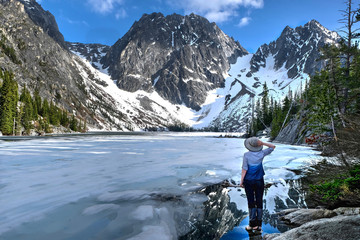 Hiking in Washington State. Woman stading by beautiful lake covered with ice. Enchantments lakes. Leavenworth. WA. United States of America.