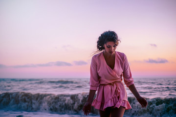 The dark-haired girl enjoys the warm sea wind at sunset, walking along the coast of the sea.