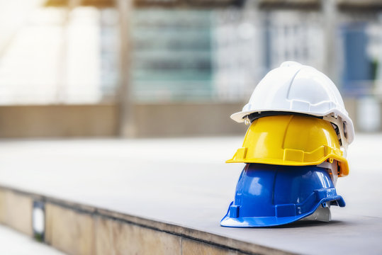 white, yellow and blue hard safety helmet hat for safety project of workman as engineer or worker, on concrete floor on city.