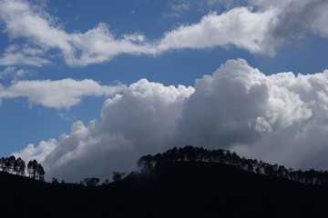 white clouds and blue sky during daytime abstract clouds above mountains filled with trees