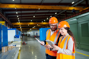 Waist up portrait of smiling female factory worker using digital tablet while discussing production...