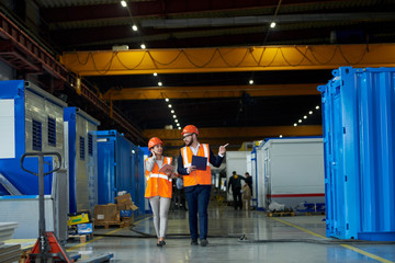 Full length  portrait of bearded businessman wearing hardhat talking to female factory worker while...