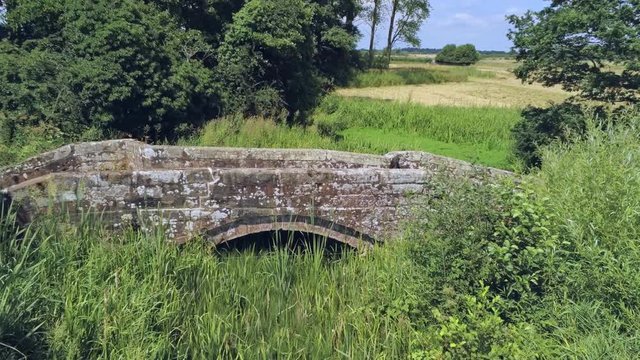 Aerial view, forward move. Fly over old small sandstone roman bridge and reed in english countryside.