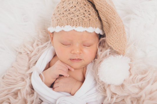 A small child in a beige knitted hat with a pompom folded his hands and sleeping