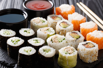 Menu set of Japanese rolls with salmon, tuna, avocado, cucumber served with sauces close-up on a stone. horizontal