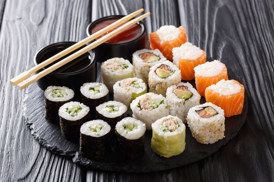 Sushi rolls set with sauces served on black slate on dark background. horizontal
