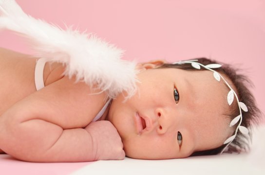Little cute Asian girl baby lying on the floor with angel wing and beautiful headband with blank copyspace