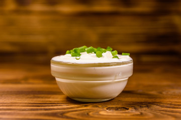 Glass bowl with sour cream and chopped green onion on wooden table