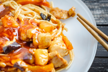 Chinese noodle udon in sour-sweet sauce with chicken and chopsticks on wooden table. Asian WOK food