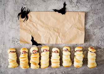 Scary sausage mummies in dough with funny eyes on table.  Halloween food. Top view. Flat lay. Banner