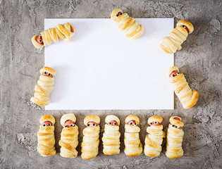 Scary sausage mummies in dough with funny eyes on table.  Halloween food. Top view. Flat lay. Banner