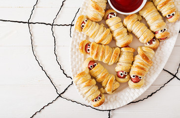 Scary sausage mummies in dough with funny eyes on table.  Halloween food. Top view. Flat lay. Banner