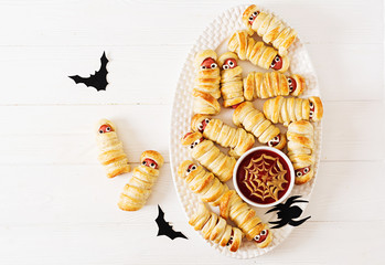 Scary sausage mummies in dough with funny eyes on table.  Halloween food. Top view. Flat lay. Banner