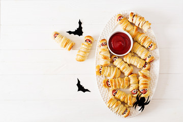 Scary sausage mummies in dough with funny eyes on table.  Halloween food. Top view. Flat lay. Banner