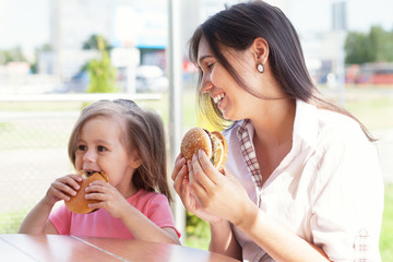 Young mother with child eating a hamburger on the street