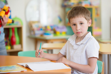 Fototapeta na wymiar Belarus, Gomel, May 4, 2018. The central kindergarten. Open day.A preschool boy at a table in class with a notebook and pen