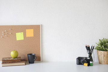 Stylish table Board and post it, book, pencil, camera  and coffee mug on table with wall.