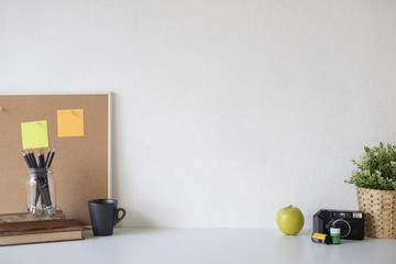 Stylish table Board and post it, book, pencil, camera  and coffee mug on table with wall.