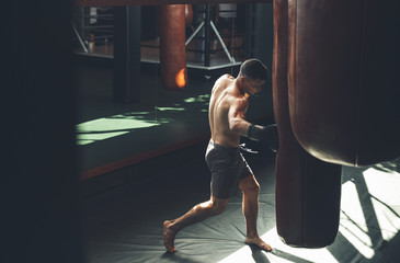 Top view of shirtless man working on kicks during workout. He is hitting punching bag with jab. He...