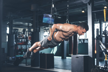 Shredded guy is feeling tension while exercising with gymnastic equipment. He is straightening all...