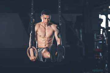 Determined guy is exercising with gymnastic outfit in gym. He is pulling up and bringing legs to parallel to the ground. Male is balancing while straining all body © Yakobchuk Olena