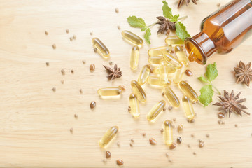 Fish oil capsules with omega 3 and vitamin D spread out of a  brown glass bottle on wooden texture, healthy diet concept.