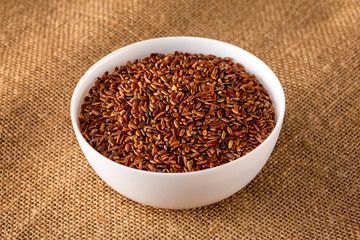 Closeup bowl of red raw rice at sack cloth background.
