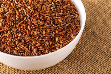 Obraz premium Closeup bowl of red raw rice at sack cloth background.