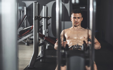 Fototapeta na wymiar Focus on joyful sportsman exercising on horizontal row machine in sport center. He is working on back muscles while using heavy weights. Copy space in left side