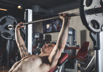 Strained athlete is doing chest press-ups with weight. He is using equipment for strength training....