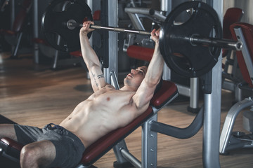 Strong sportsman is exercising with machine and barbell. He is lying on bench and lifting weight. Training with equipment concept