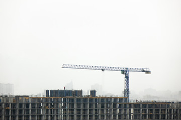 Construction crane against the cloudy background and the silhouettes of buildings in the misty sky.