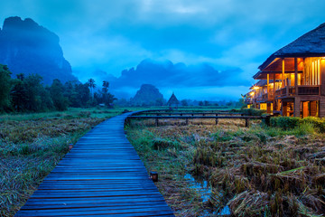 Beautiful landscape of Wooden path on surrounded by rice fields and towering mountains with mist, Vang Vieng, Laos, is one of Southeast Asia's most beautiful adventure destinations in Dawn time