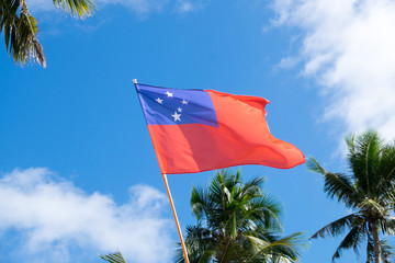 Flag of Western Samoa flying against a blue sky with clouds and palm trees
