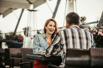Happy meeting. Cheerful young woman looking at man and laughing. Couple sitting at the table with glass of water