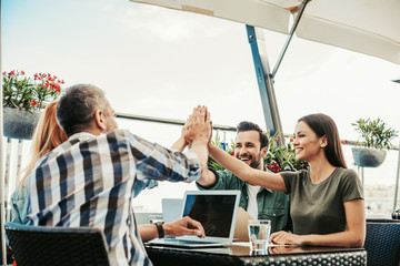 Celebrating success. Bearded men and beautiful young ladies giving high five. Couples sitting at the table with laptops and glasses of water