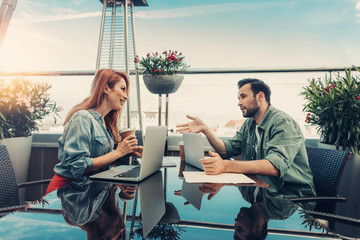 Nice meeting. Attractive lady and bearded man discussing work at rooftop cafe