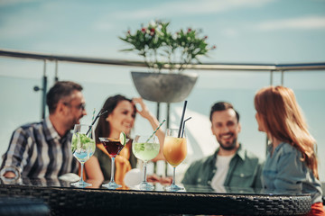 Having fun. Cocktails with straws standing on the table of rooftop bar. Two young couples chatting and smiling