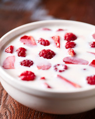 White bowl with helthy breakfast with fresh ripe berries and yoghurt on a wooden table.