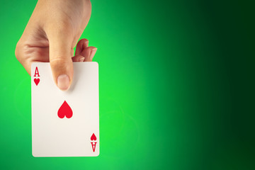 A hand holding an ace of hearts against a green background with copyspace