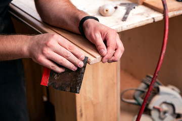 Close-up A young male carpenter in a purple shirt removes excess packaging and equips a wooden door with a spatula in the workshop